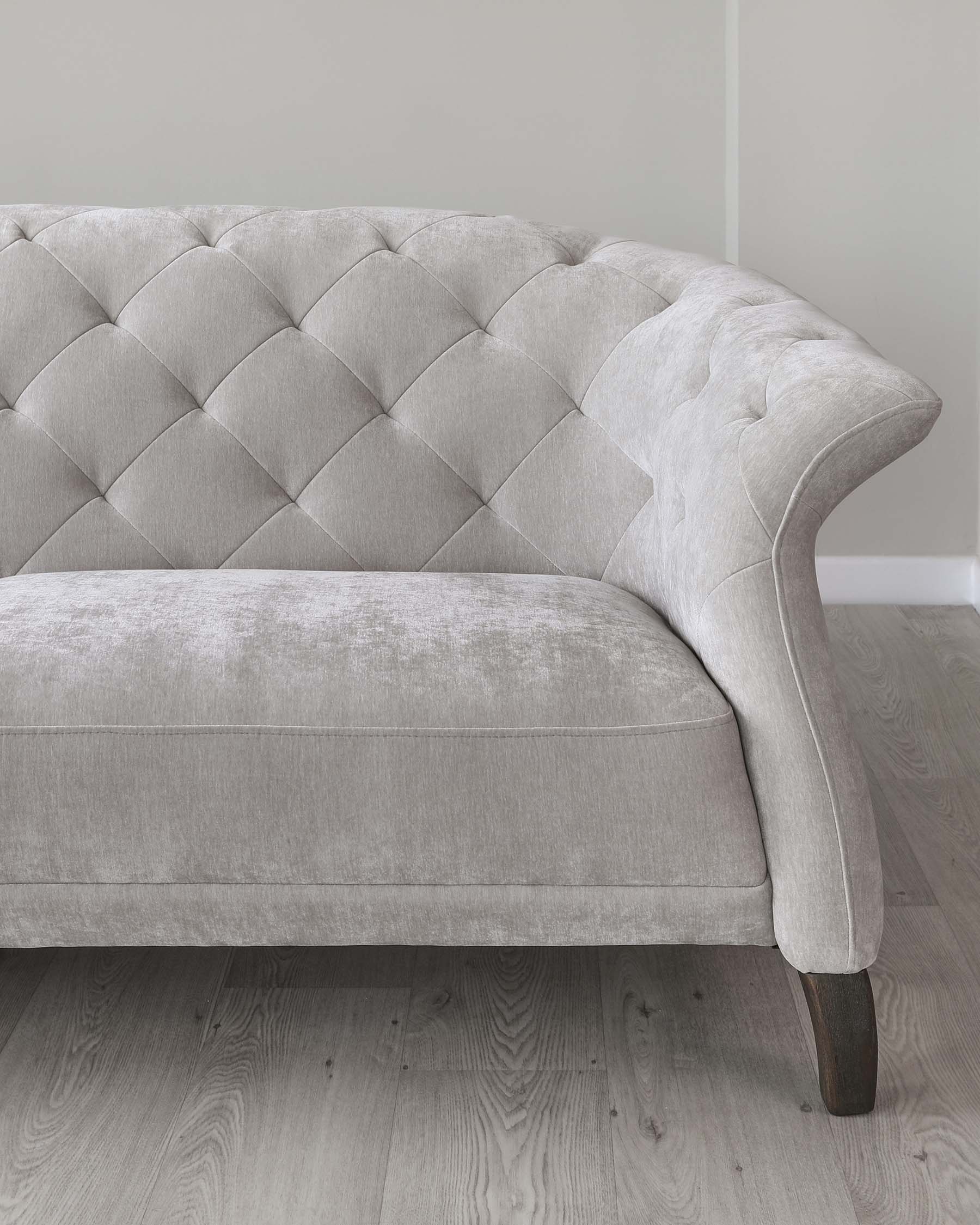 Elegant grey fabric sofa with tufted backrest and scrolling arms, featuring dark-stained wooden legs, placed on a light wooden floor against a grey wall.