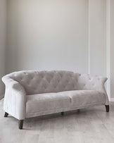 Elegant light grey tufted fabric sofa with curved armrests and dark wooden legs on a light hardwood floor against a neutral wall background.