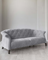 Elegant grey fabric sofa with tufted backrest and contoured armrests, standing on dark wooden legs with a light wood flooring background.