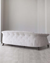 Elegant modern curved sofa in off-white with geometric stitching detail, displayed in a minimalistic interior with light hardwood flooring.