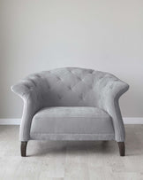 Elegant grey tufted loveseat with a curved back, scroll arm design, and dark wooden legs, set against a light wooden floor and a plain white wall.