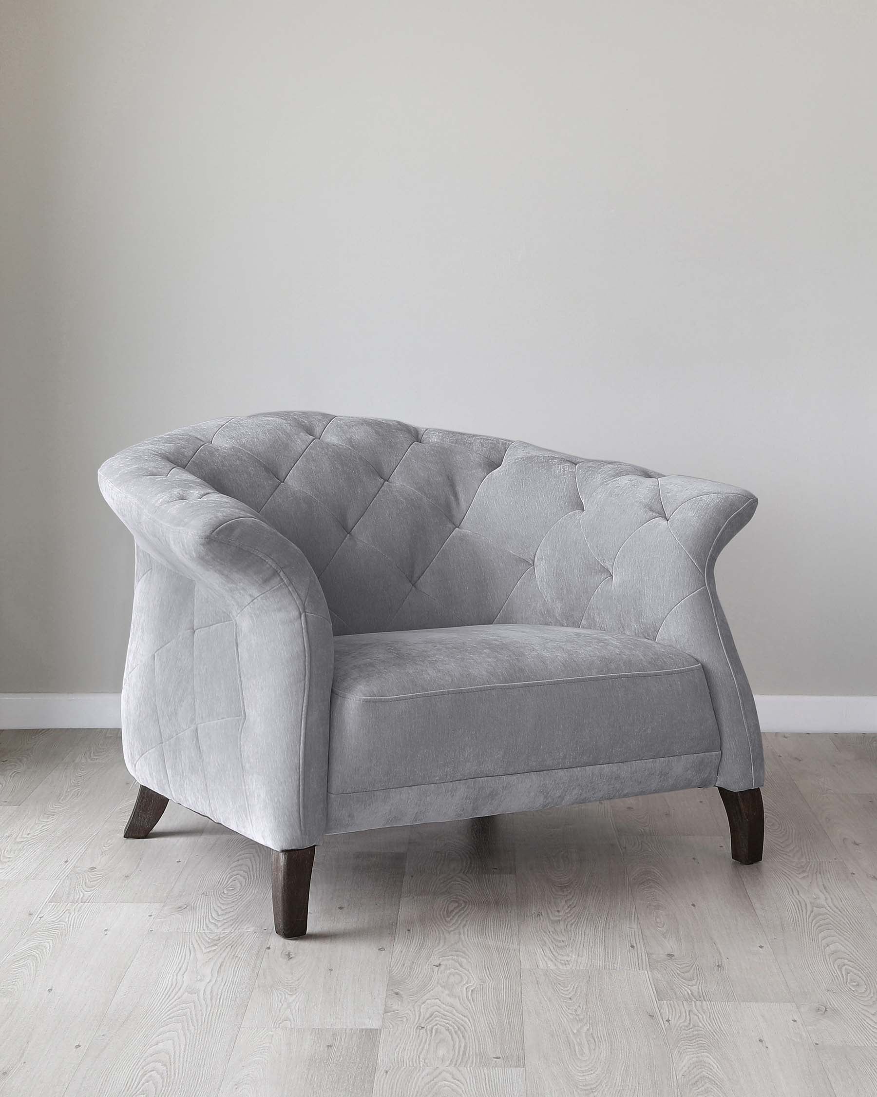 Elegant grey velvet loveseat with tufted backrest and curved armrests, supported by dark wooden legs, against a white wall on light hardwood flooring.