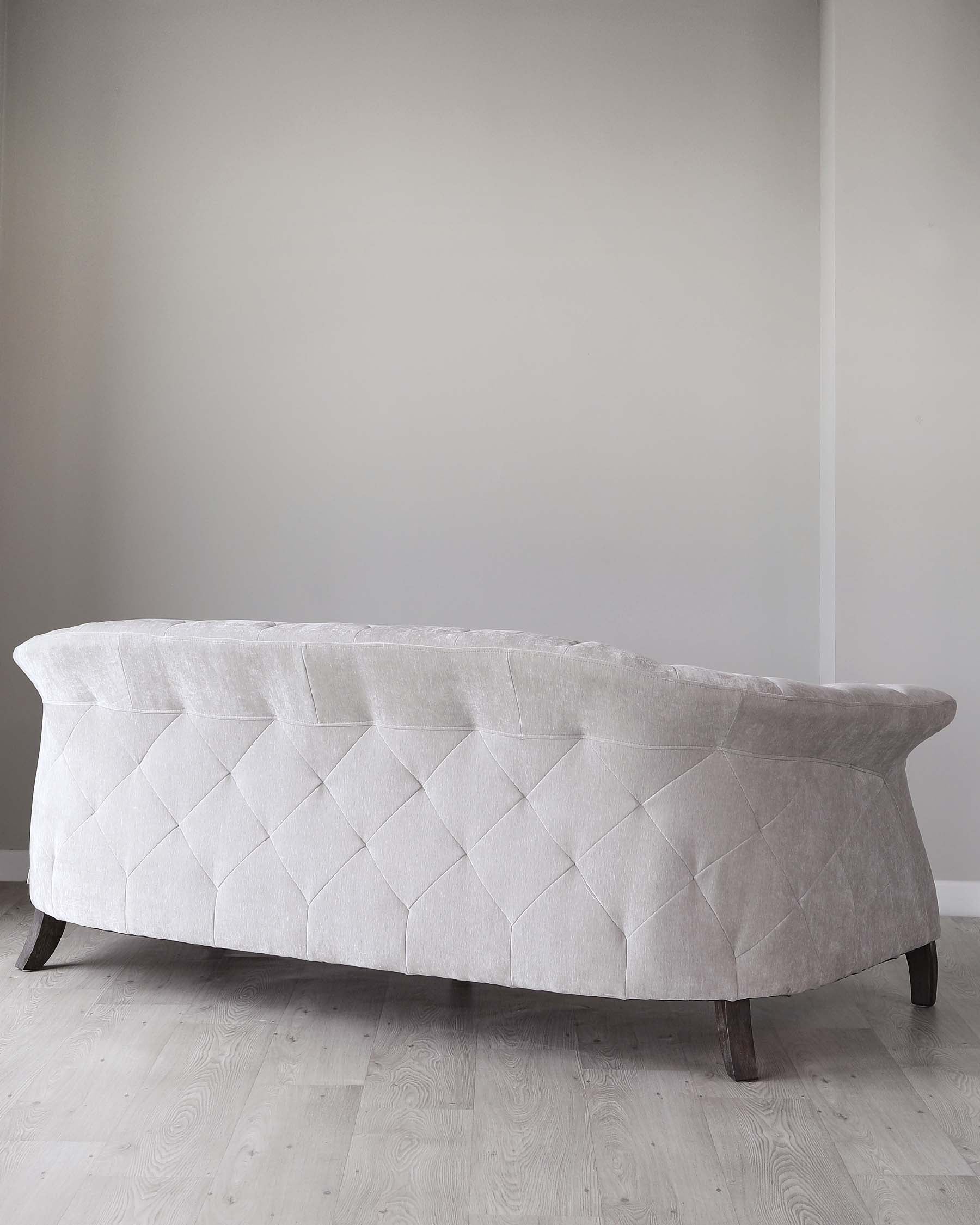 Elegant contemporary sofa with a curved silhouette, featuring a tufted back upholstered in light grey fabric, and supported by dark wooden legs.