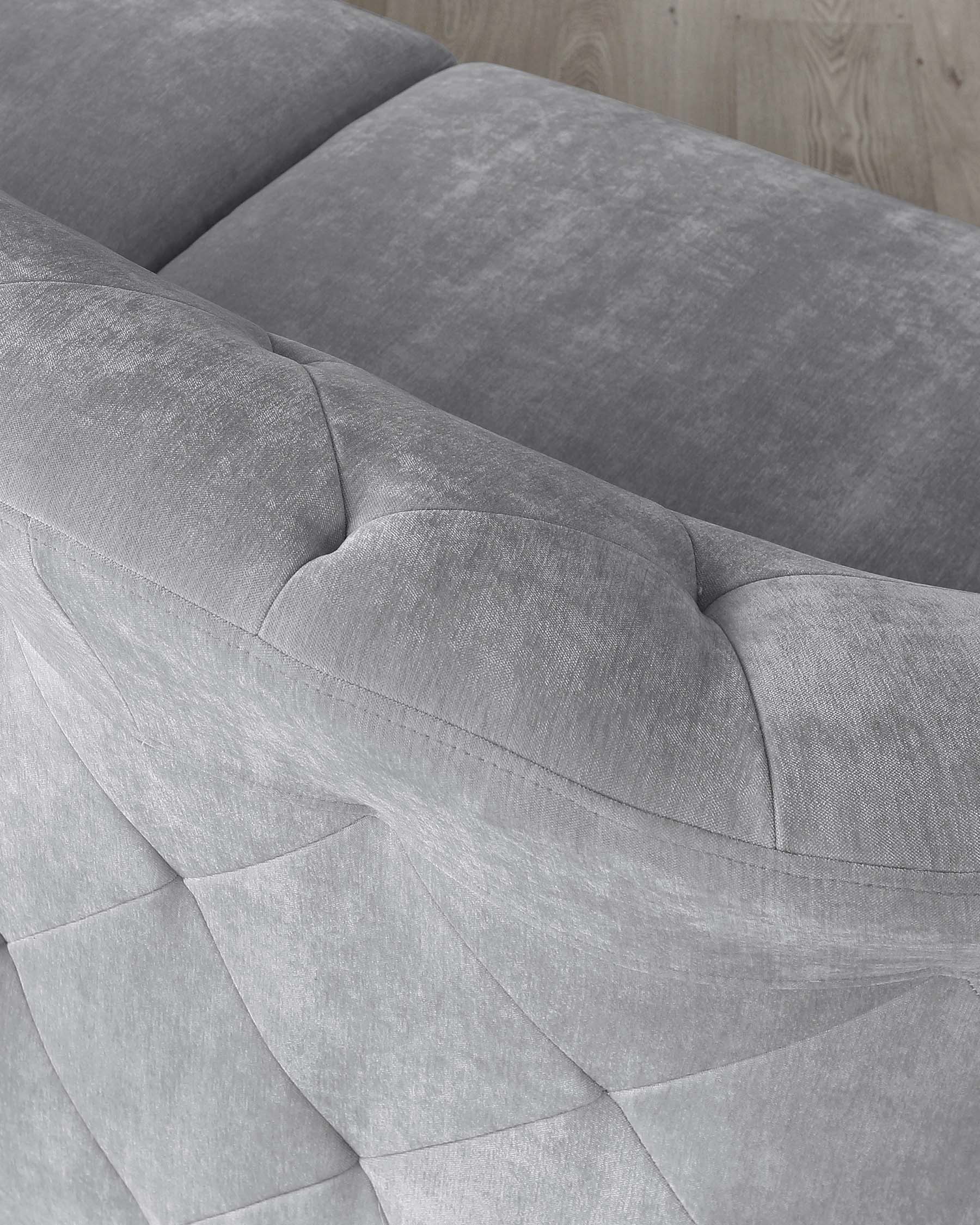 Close-up of a modern light grey fabric sofa showcasing a smooth texture and elegant seam details on the backrest and seating area, set against a backdrop of a wooden floor.