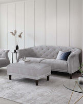 Stylish gray tufted sofa with a matching ottoman, accompanied by a glass side table and decorative accents on a textured rug.