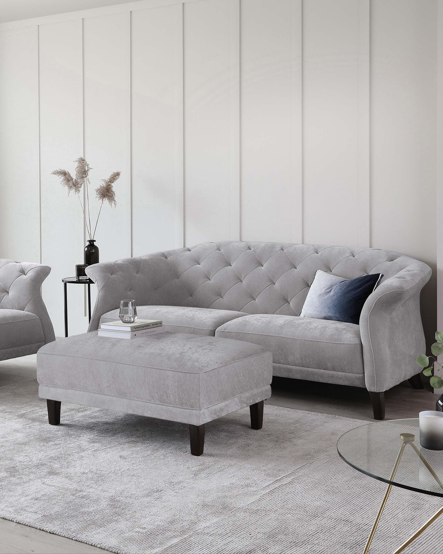 Stylish gray tufted sofa with a matching ottoman, accompanied by a glass side table and decorative accents on a textured rug.