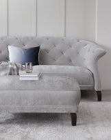 Contemporary grey tufted sofa with elegant curved arms, paired with a plush ottoman and accented by a decorative pillow.