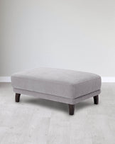 A soft gray fabric ottoman with a sleek design and dark wooden legs, perfect for adding comfort and style to any room.