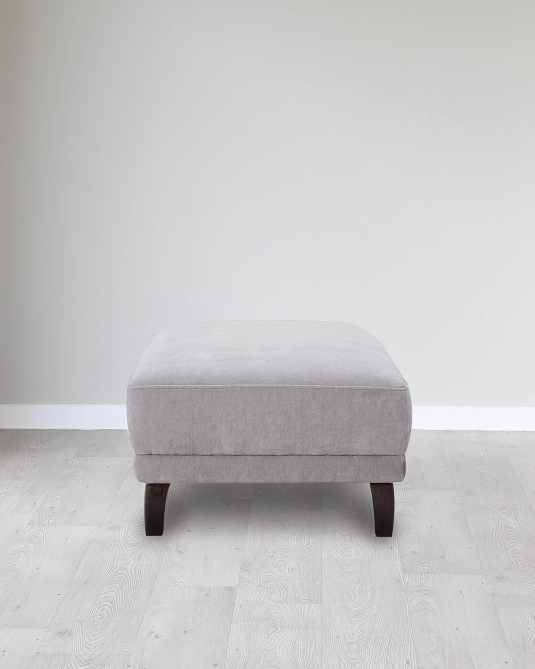 A modern, square, light gray upholstered ottoman with dark wood legs, set against a minimalist background.