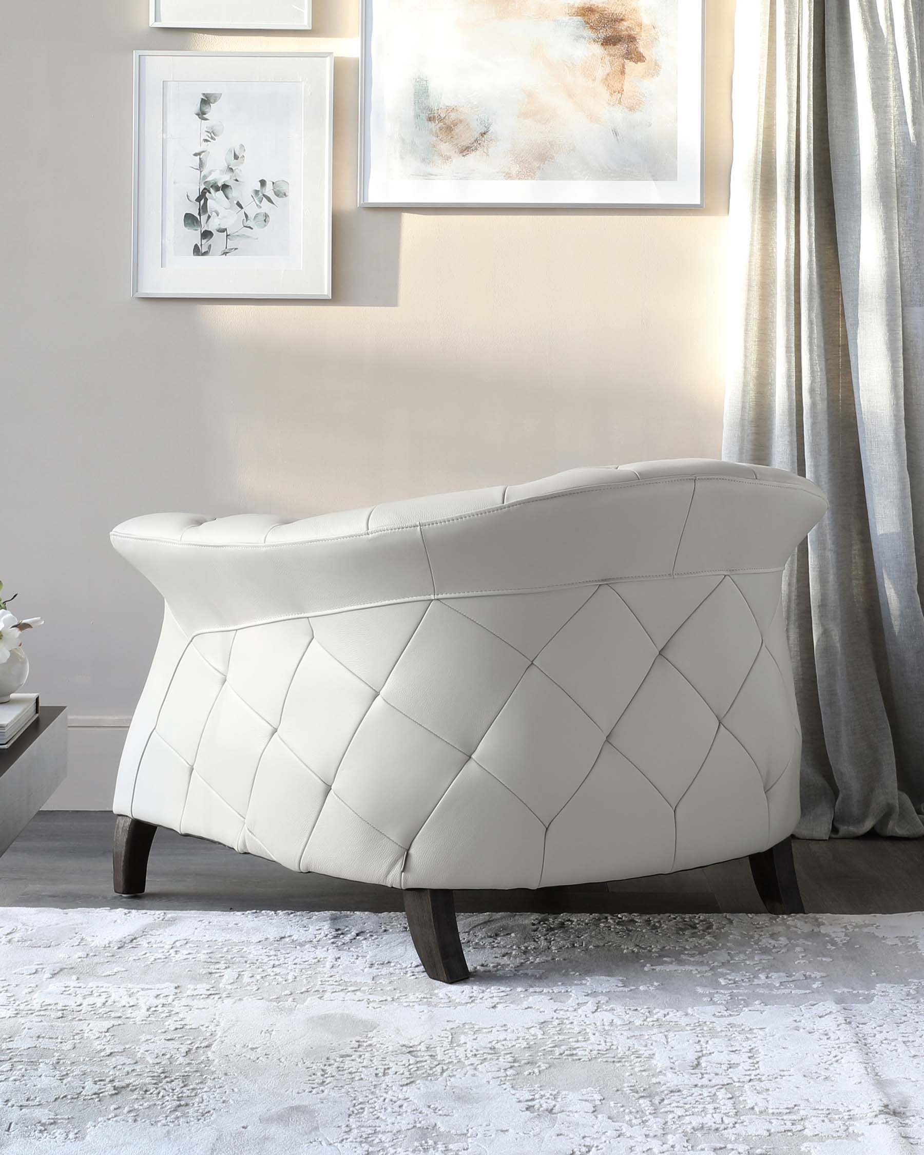 Elegant tufted light grey loveseat with a unique curved back design and dark wooden legs, set against a light modern interior with artwork and drapery.