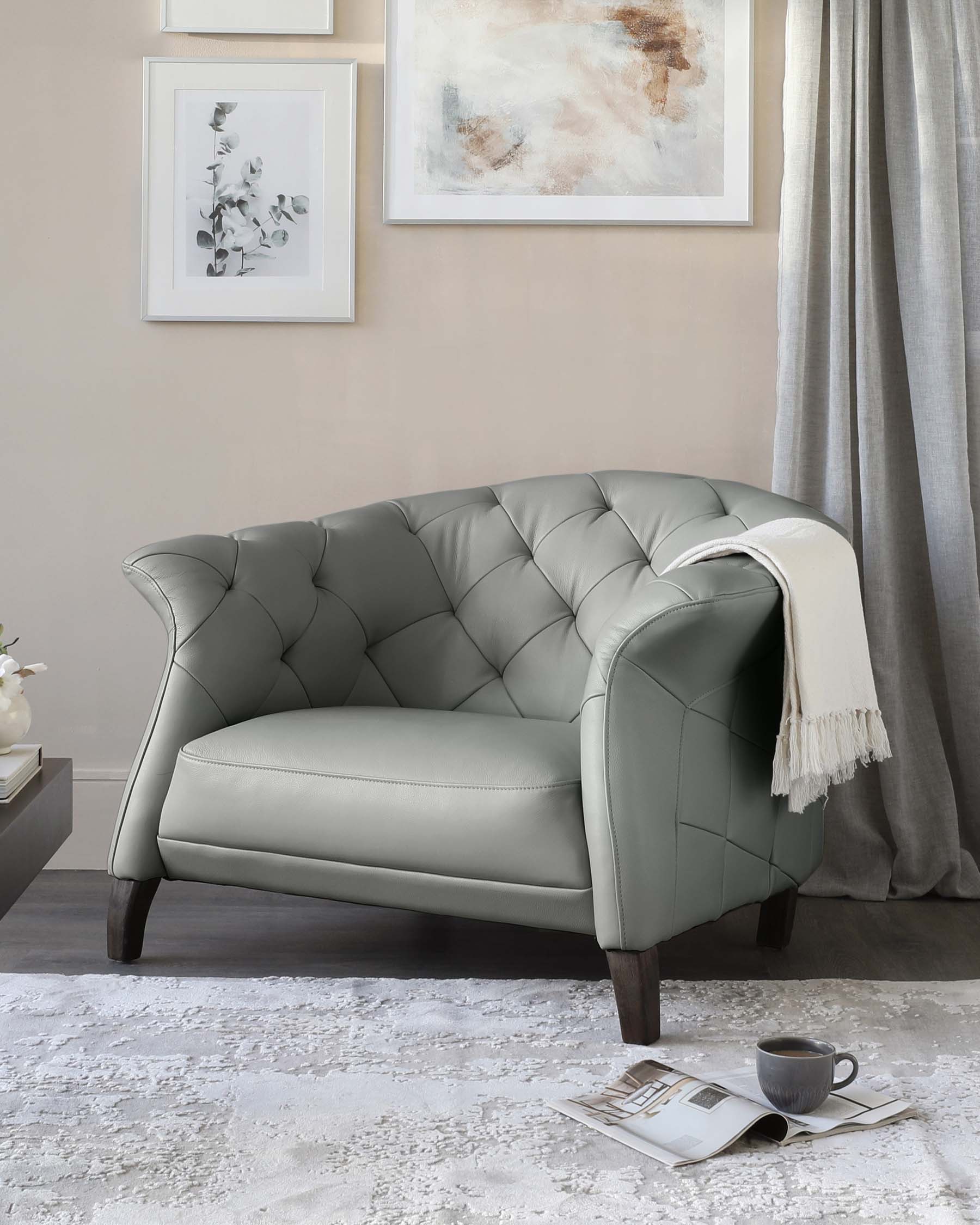 Elegant grey tufted loveseat with dark wooden legs, featuring a smooth leather finish and a plush throw blanket draped over one arm.