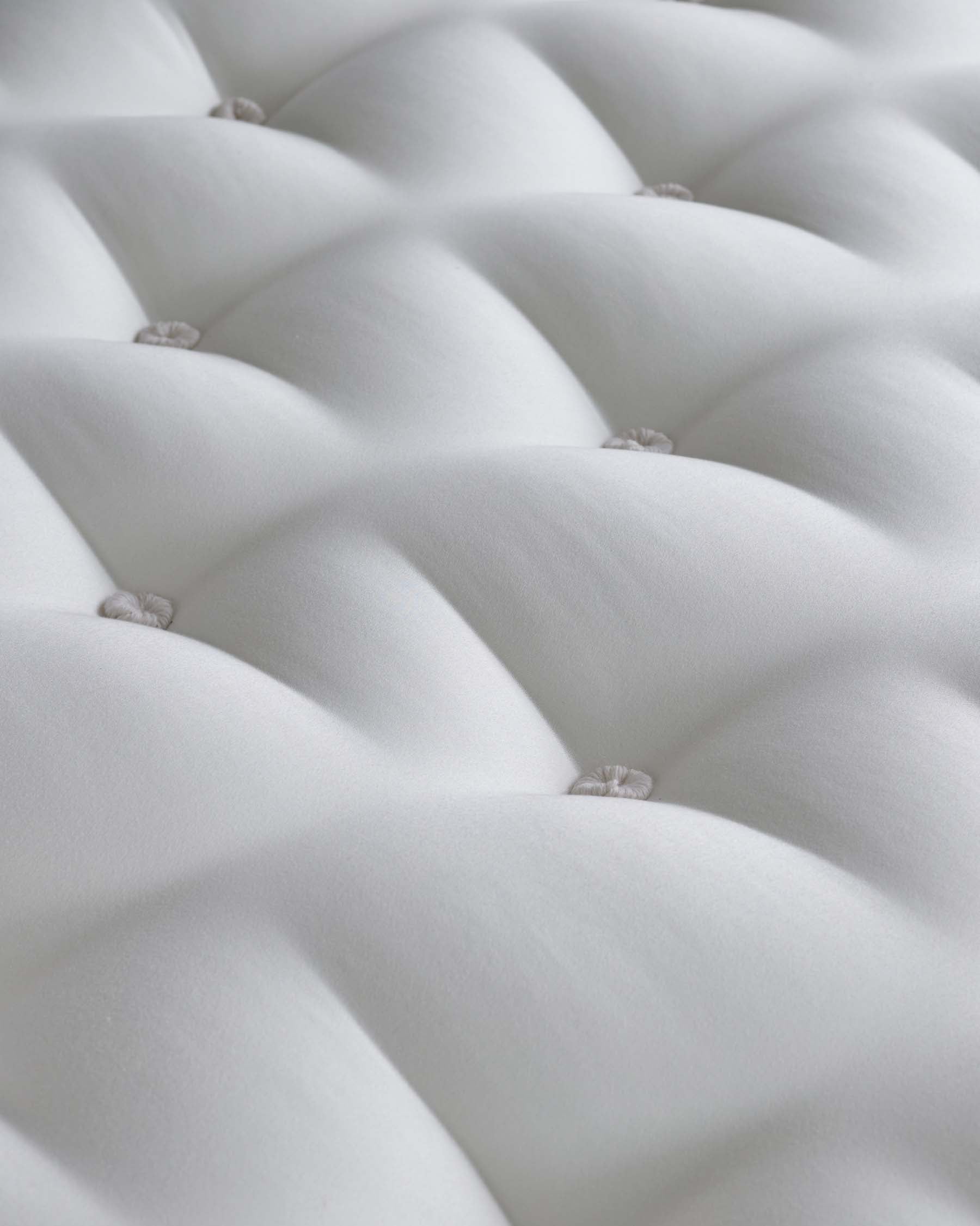 Close-up of a white tufted upholstery fabric with button details suggesting a luxurious and elegant piece of furniture such as a sofa or headboard.