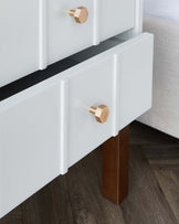 Modern white drawer cabinet with hexagonal wooden knobs and a contrasting black inner drawer section, standing on a rectangular dark wooden leg, displaying a minimalist and contemporary design.