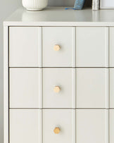 Modern white dresser with a minimalist design, featuring multiple drawers with simple geometric wooden knobs.