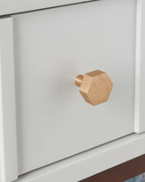 A close-up of a modern white drawer featuring a geometric brushed gold knob.