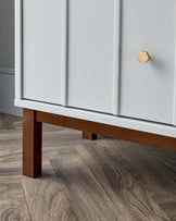 Close-up of a modern cabinet with white doors and a wooden hexagonal knob, featuring a sturdy brown wooden leg supporting one corner.