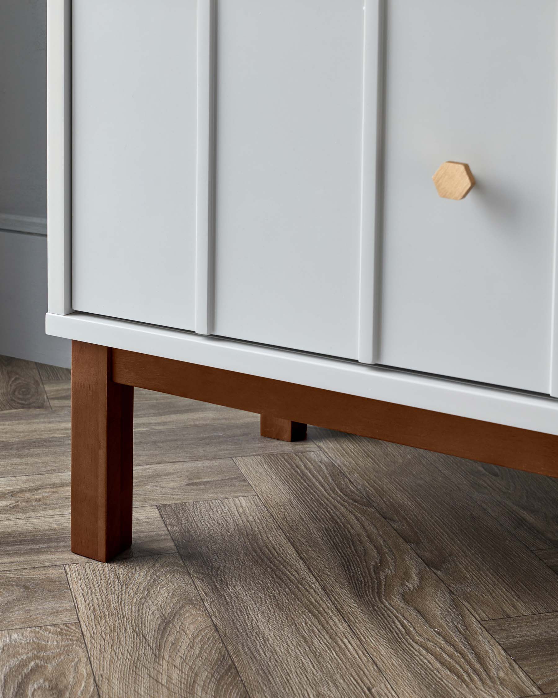 Close-up of a modern cabinet with white doors and a wooden hexagonal knob, featuring a sturdy brown wooden leg supporting one corner.