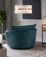 Plush velvet rounded armchair in deep teal, featuring a smooth curved back and a contemporary design, set against a modern room decor with a minimalist side table and chic hanging lamp.