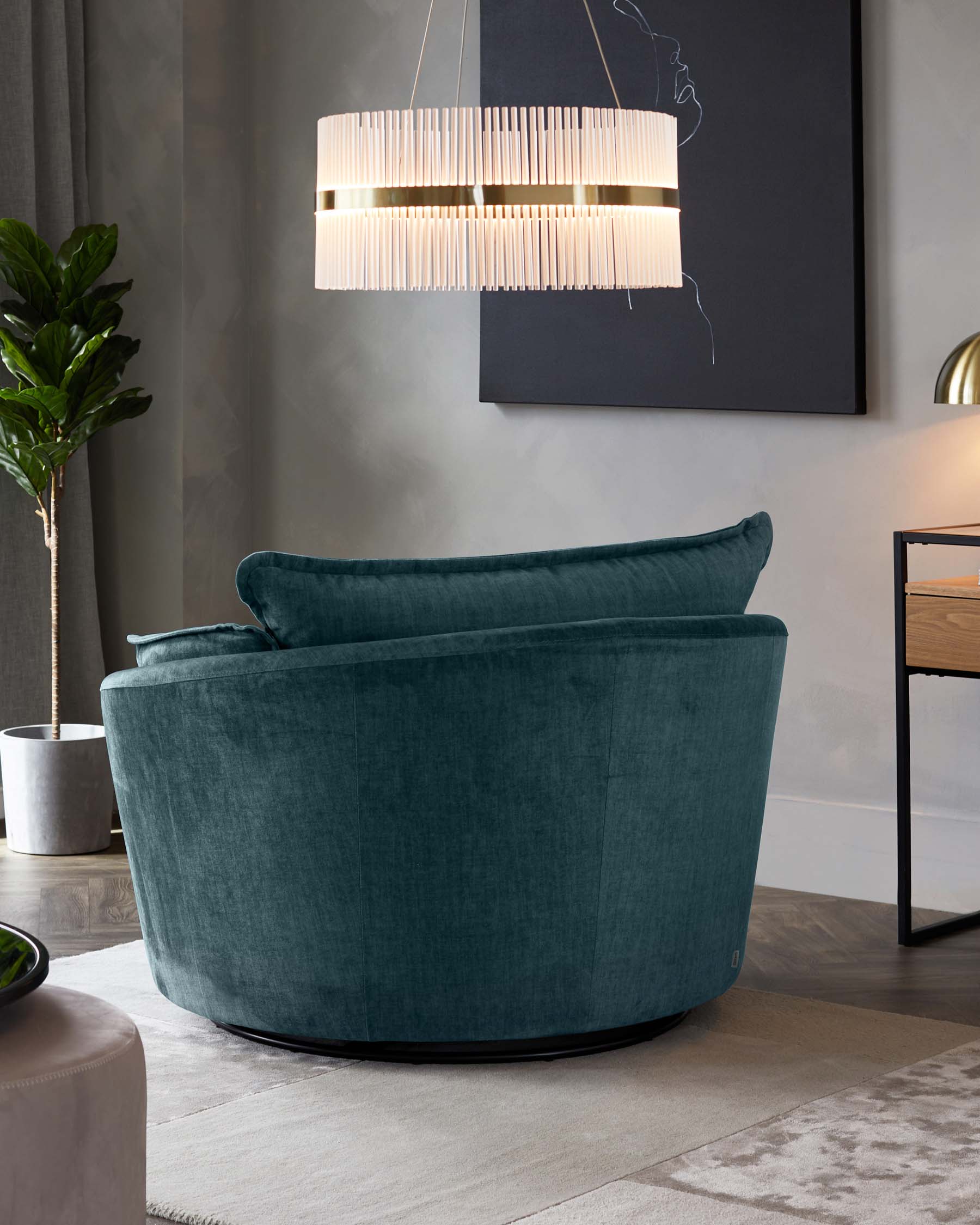 Plush velvet rounded armchair in deep teal, featuring a smooth curved back and a contemporary design, set against a modern room decor with a minimalist side table and chic hanging lamp.