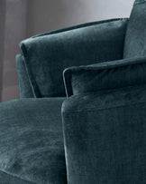 Close-up of a luxurious teal velvet sofa with plush cushions and a smooth, soft texture. The furniture has a modern silhouette with clean lines and an inviting appearance.