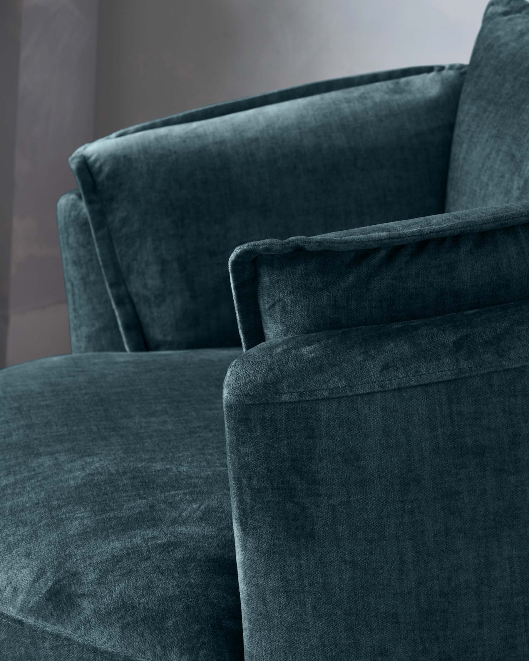 Close-up of a luxurious teal velvet sofa with plush cushions and a smooth, soft texture. The furniture has a modern silhouette with clean lines and an inviting appearance.