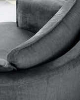 Close-up of a plush, upholstered armchair in a textured grey fabric with a rounded armrest and an elegant throw pillow along the backrest.