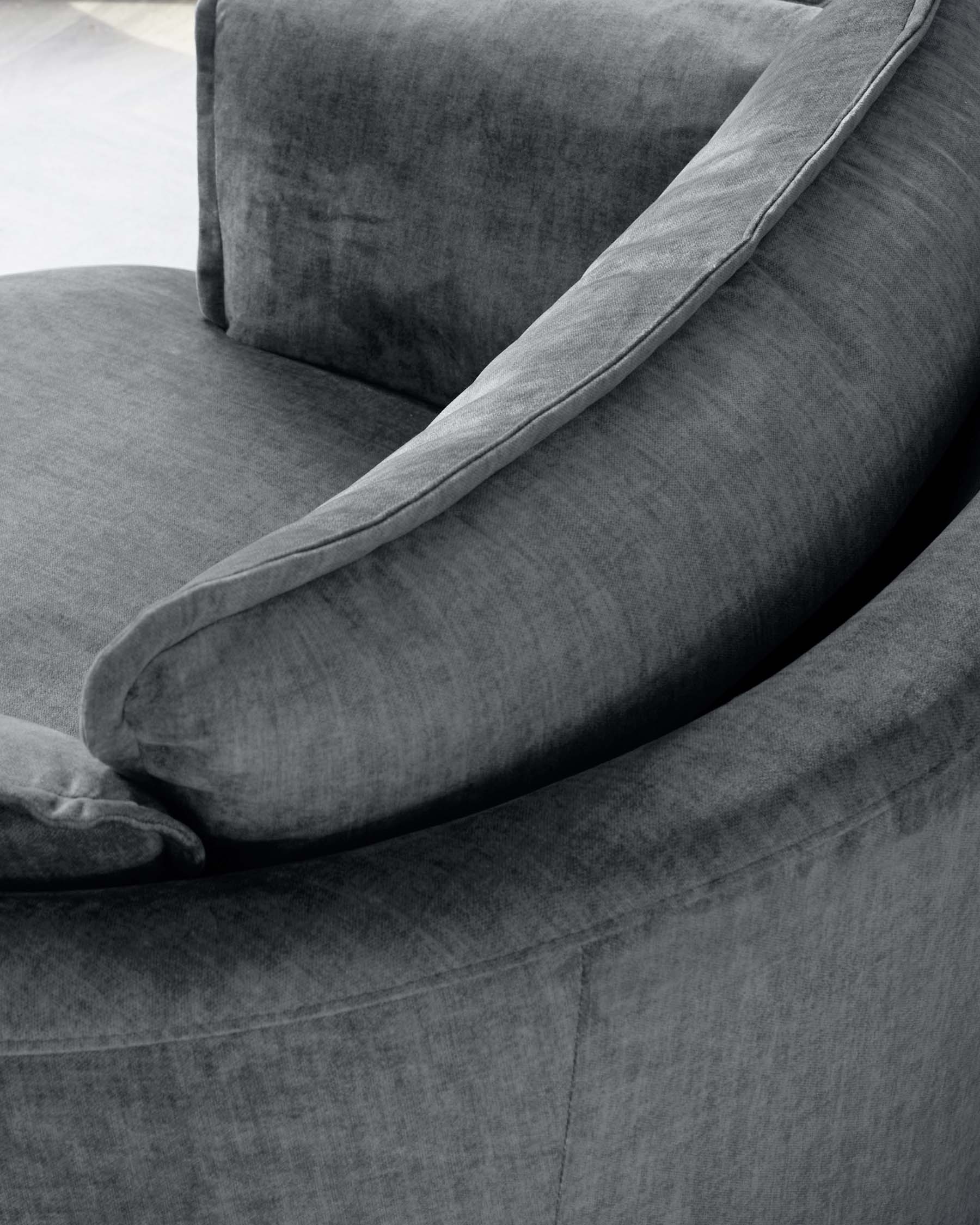 Close-up of a plush, upholstered armchair in a textured grey fabric with a rounded armrest and an elegant throw pillow along the backrest.