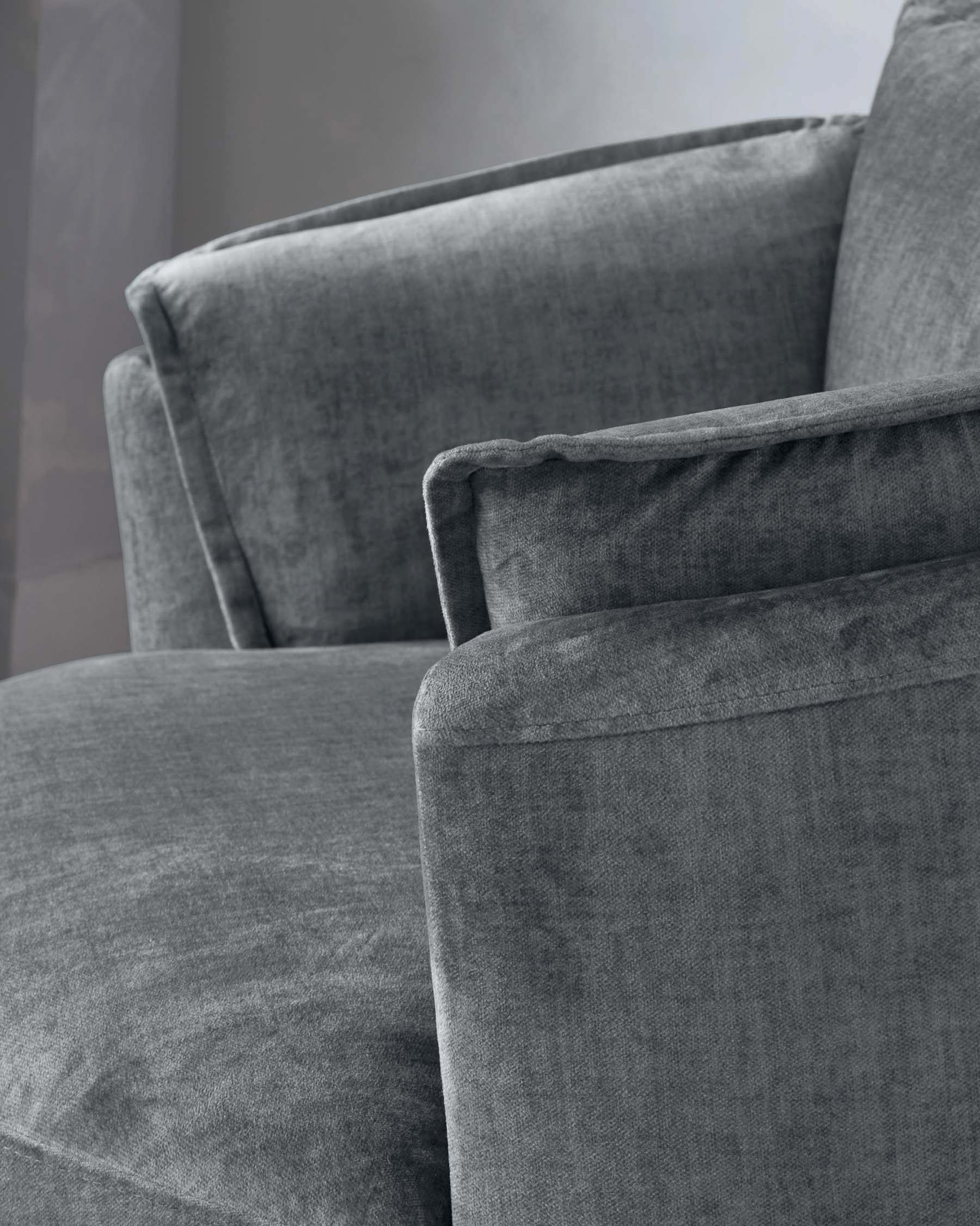 Close-up view of a modern charcoal grey upholstered armchair with soft fabric texture, showcasing the comfortable seat cushion and supportive backrest with a slightly curved top edge.