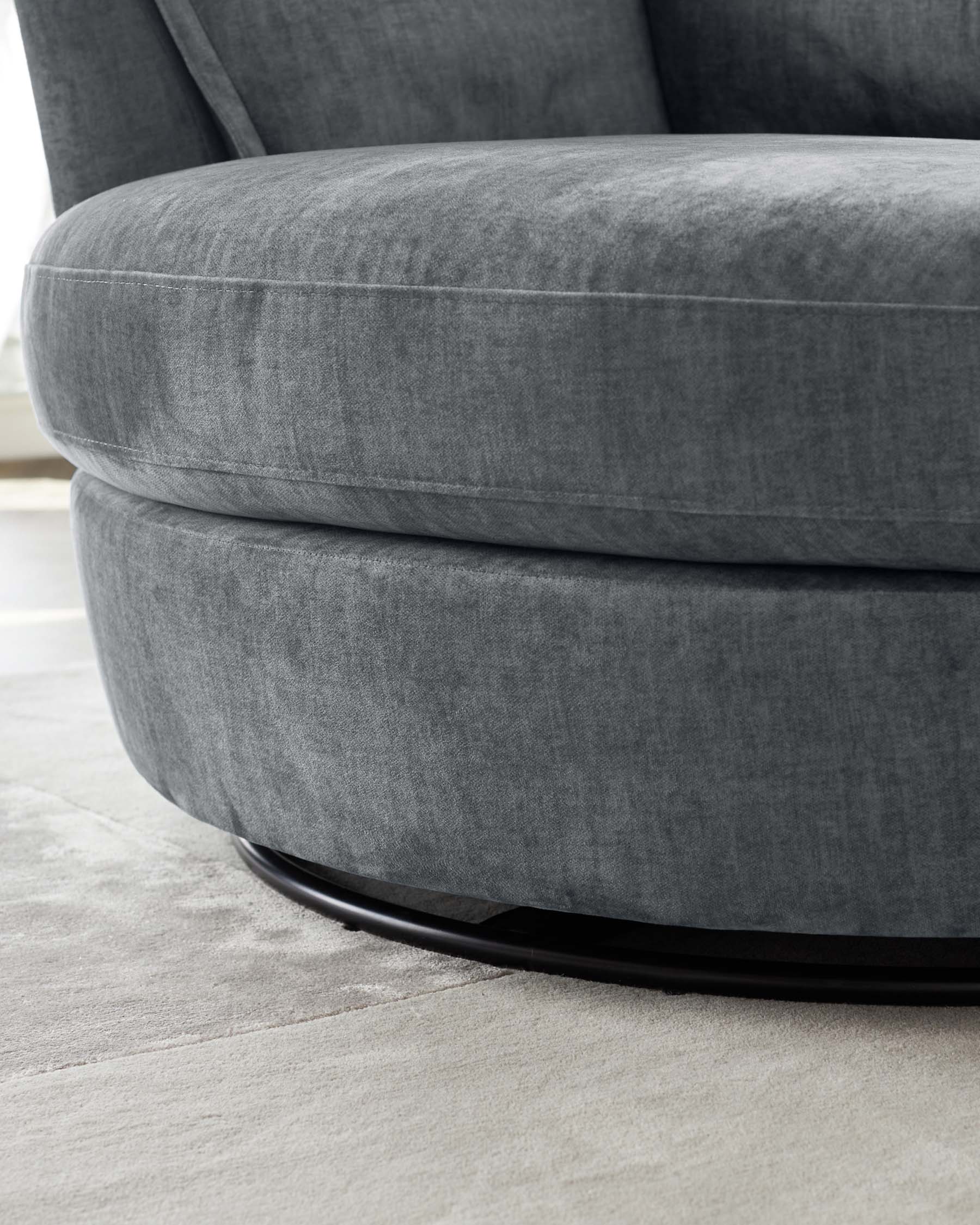 Luxurious modern rounded armchair with plush velvet upholstery in a sleek graphite grey, featuring a subtly tufted cushion design and an elegant black circular base.