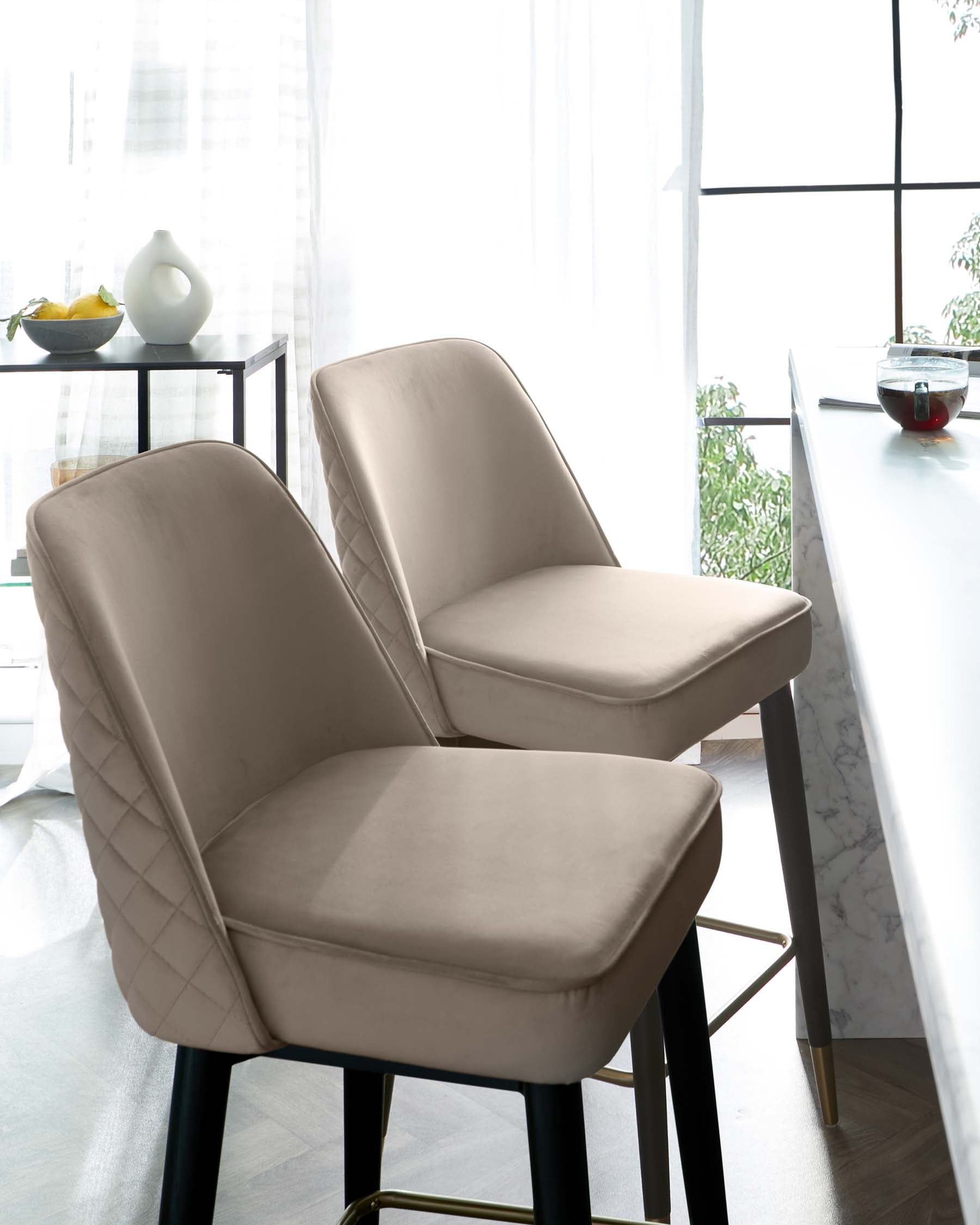 Two modern upholstered dining chairs with beige fabric and a diamond tufted backrest design. The chairs feature sleek black metal legs with gold accents at the base.