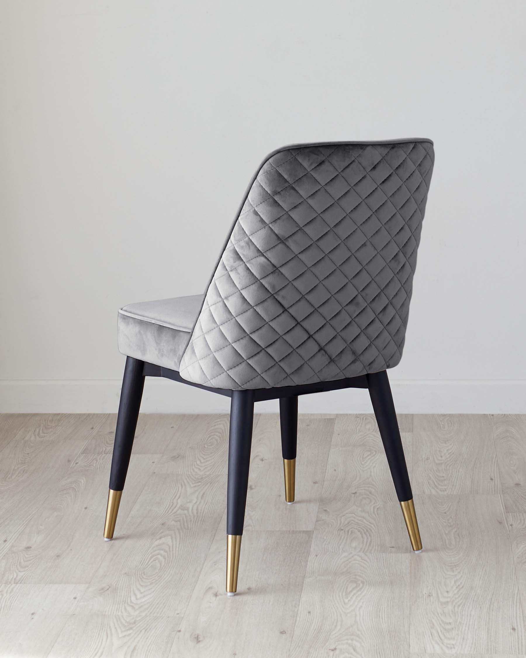 Elegant modern dining chair with a grey quilted fabric upholstery and contrasting black legs with gold-tone metal tips, against a neutral background.