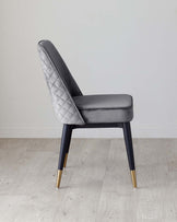 Elegant modern dining chair with a grey quilted leather back and seat, tapered black legs with gold metal tips, displayed on a light hardwood floor against a neutral wall.