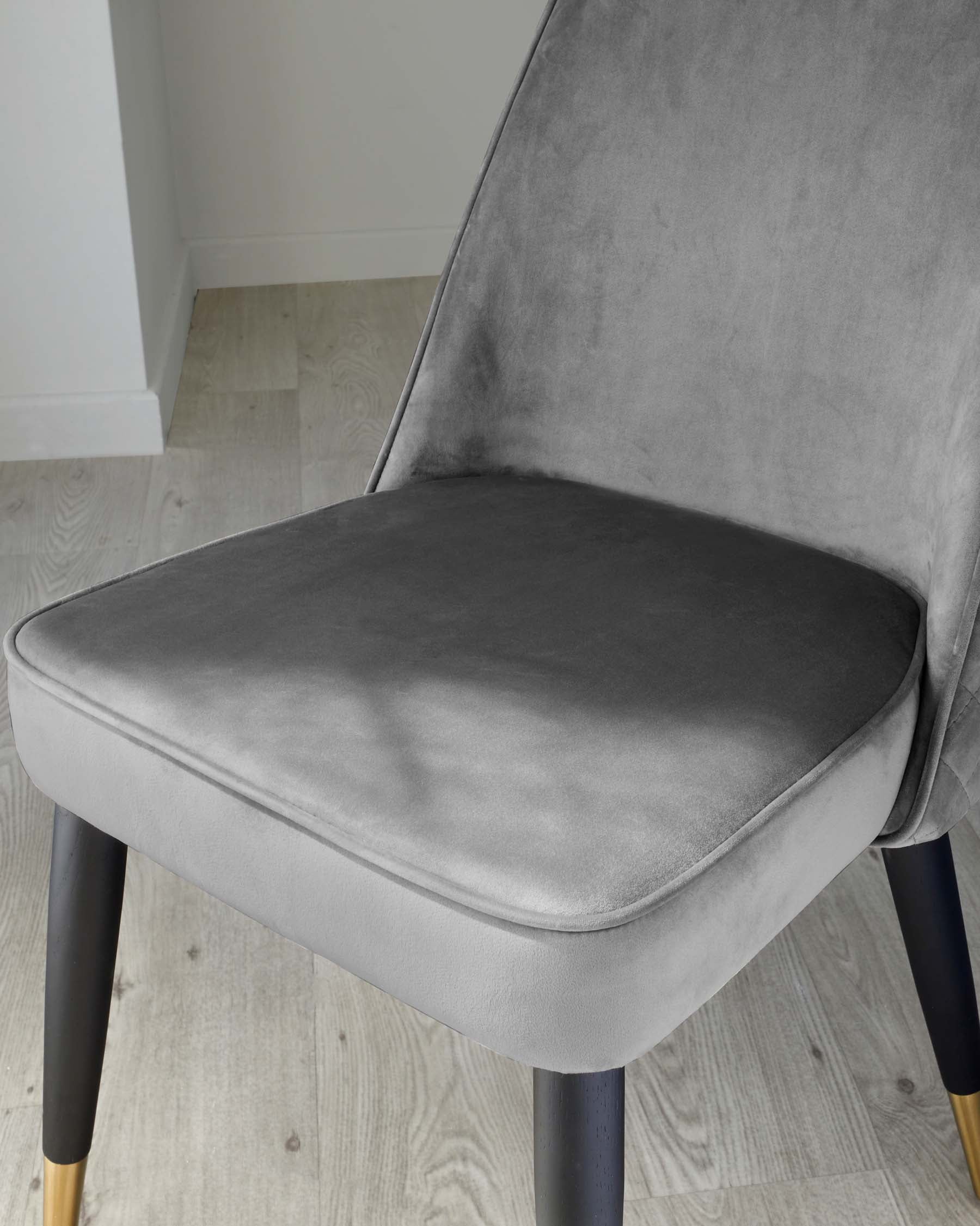 Modern minimalist dining chair with plush grey velvet upholstery and black wooden legs accented with gold tips, featuring a slightly curved backrest for added style and comfort.