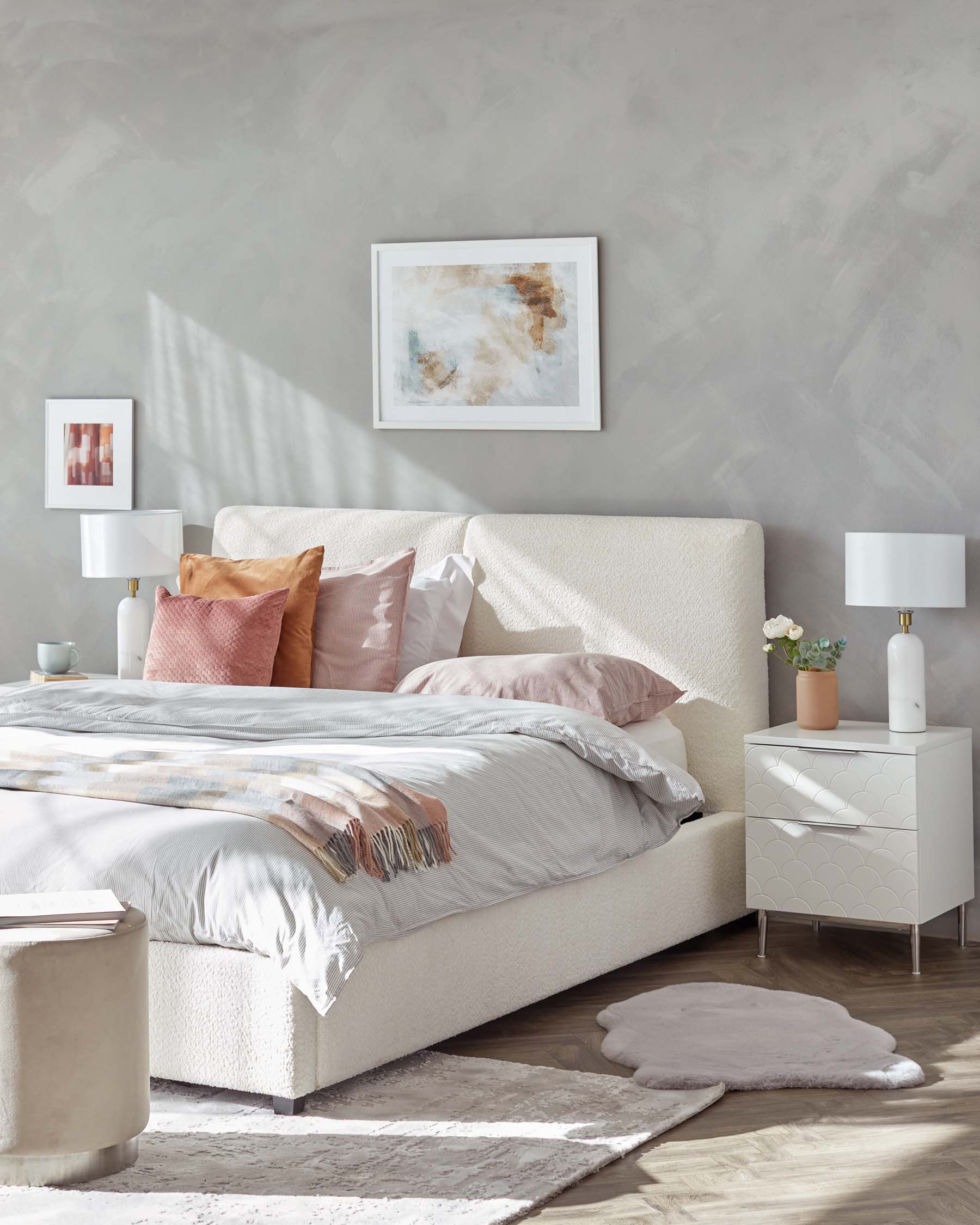 Elegant bedroom featuring a modern upholstered bed with a textured headboard, accompanied by two sleek white bedside tables with stylish curved details and metal legs. Coordinating with the serene decor, a contemporary drum-shaped ottoman completes the sophisticated look.