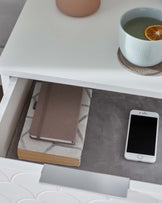 Modern minimalist white side table with sleek lines and an open shelf, displaying an assortment of items.