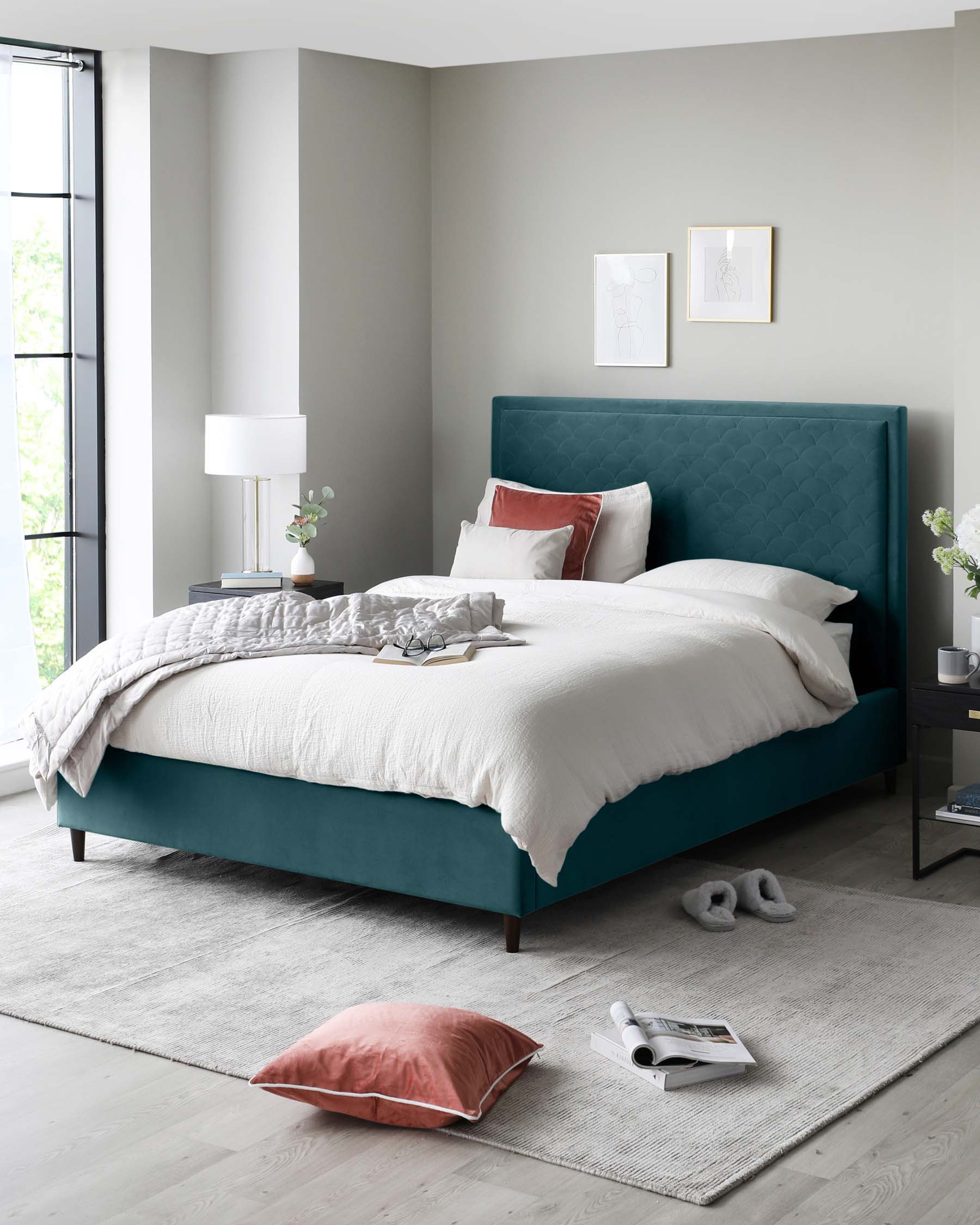 A luxurious teal upholstered queen-size bed with a tall tufted headboard, white bedding, and accent pillows, flanked by a dark wood nightstand with a stylish white lamp, all resting on a large grey area rug.