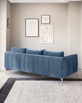 Elegant contemporary blue fabric sofa with a tufted backrest and sleek metallic legs, positioned on a two-tone grey area rug in a minimalist styled room.