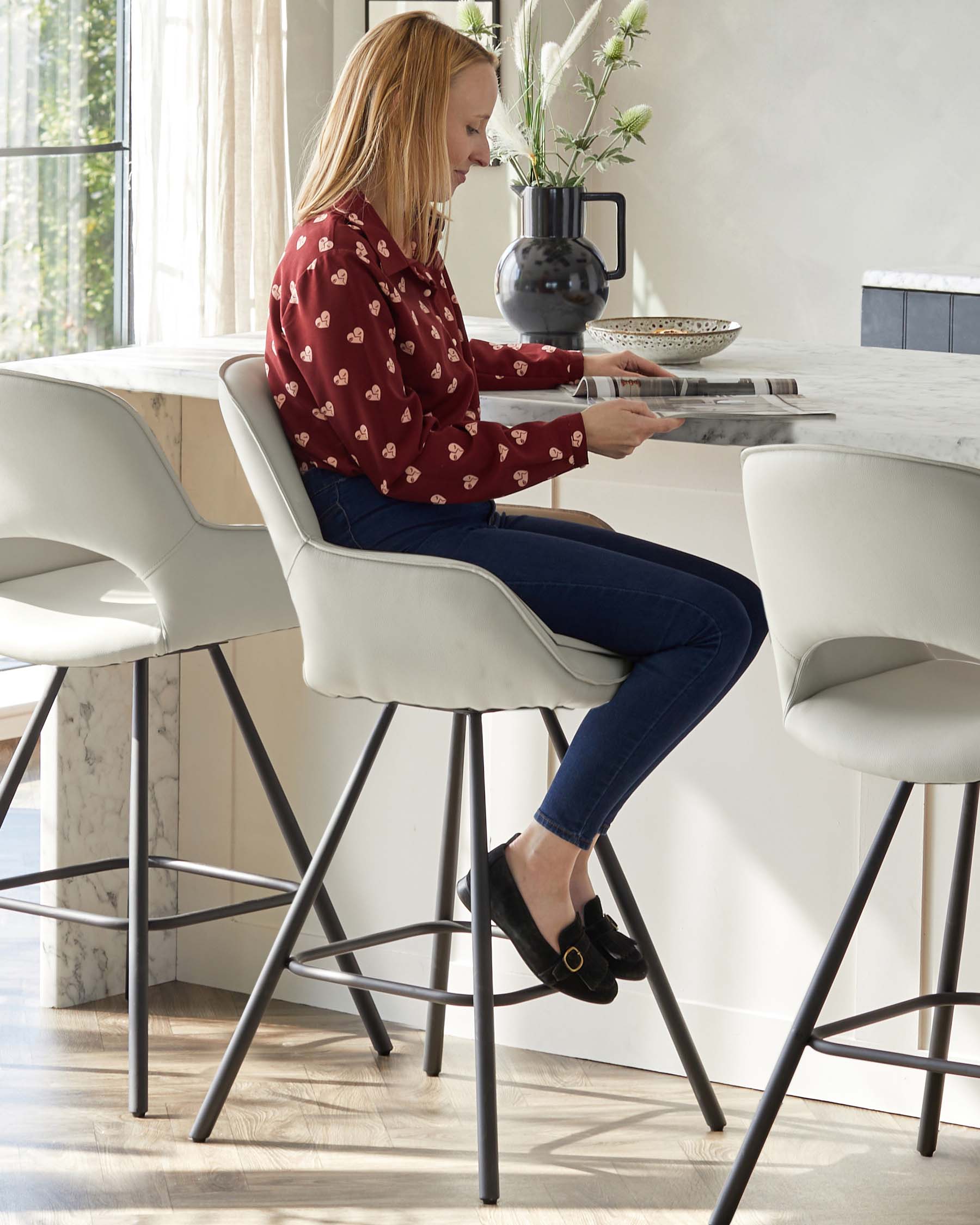 Modern minimalist bar stools with cream upholstery and slim, black metal legs, paired with a marble top kitchen island featuring a subtle grey vein design.