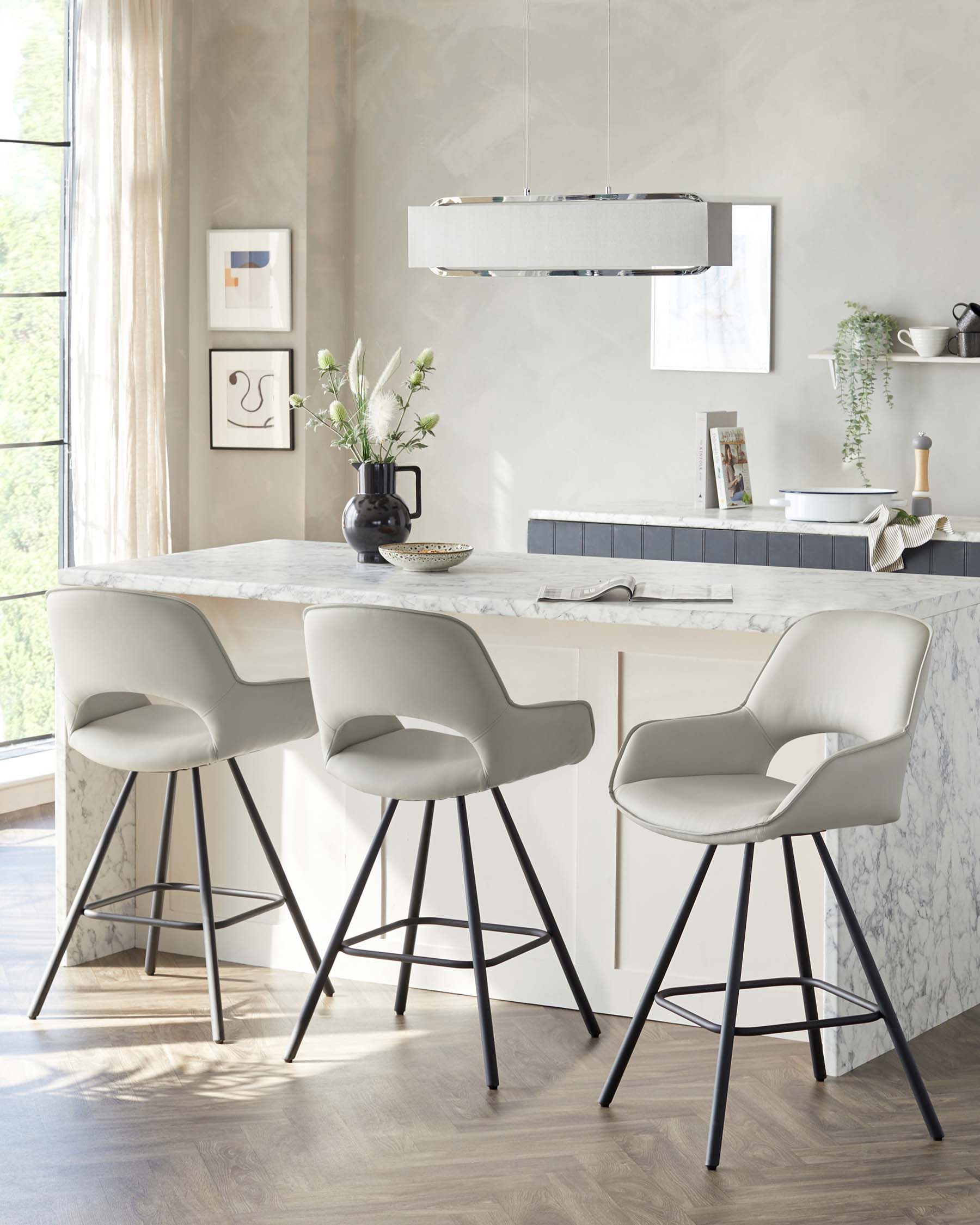 Modern light grey upholstered bar stools with low backs and black metal legs arranged around a white marble kitchen island counter.