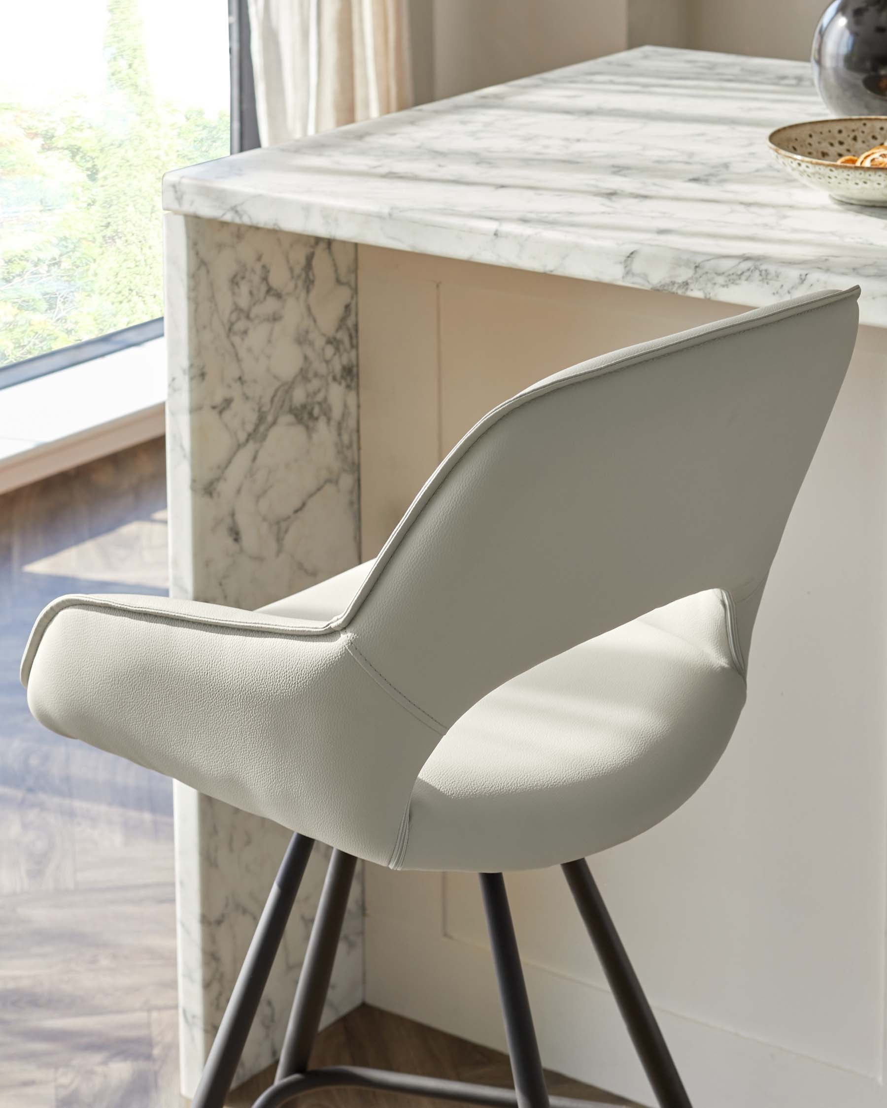 Modern dining chair with a contoured, light grey upholstered seat and matte black metal legs, paired with a kitchen island featuring a white marble countertop.