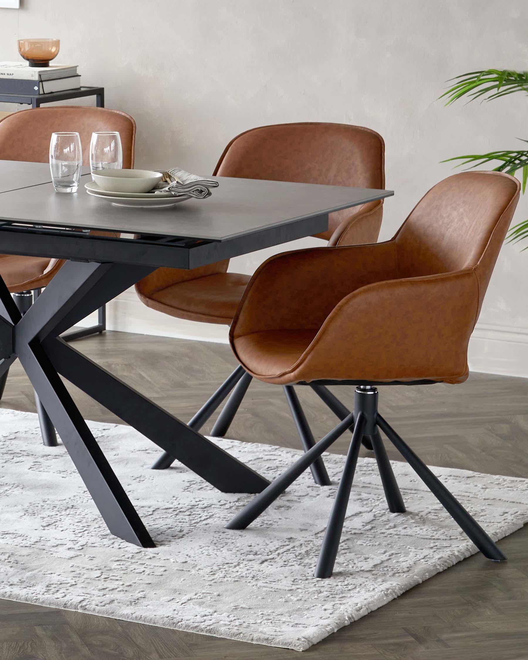 Modern dining room set featuring a rectangular table with a sleek grey finish and a stylish black X-base design, paired with three mid-century inspired chairs with smooth tan leather upholstery and black metal legs. A contemporary textured white area rug underlines the arrangement.