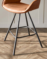 Modern bar stool with sleek metal legs and a caramel brown leatherette seat with a supportive backrest.