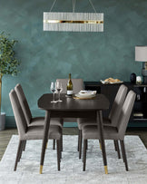 Modern dining room featuring a dark wood circular table and four taupe upholstered chairs with high backs and wooden legs tipped with golden accents on a white textured rug. A contemporary chandelier with horizontal metallic bars hangs overhead.