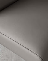 Close-up of a modern charcoal grey leather sofa with fine stitching detail and a soft texture, set against a light wooden floor background.