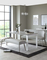 Modern minimalist dining room furniture set featuring a sleek white rectangular table with a glossy finish and metal legs, paired with two elegant grey upholstered chairs with a high back and slim legs, complemented by a matching grey upholstered bench. The set is arranged on a grey textured area rug.