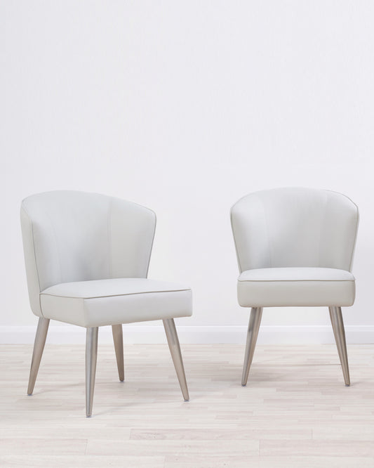 Two contemporary light grey upholstered armchairs with angled wooden legs set against a neutral backdrop.