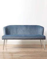 Elegant contemporary blue velvet sofa with a curved back and silver metal legs against a white wall on a hardwood floor.