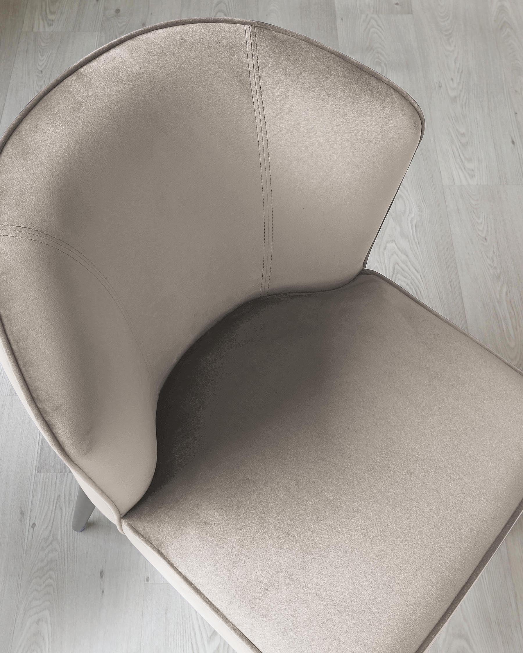 Modern minimalist chair with a smooth beige upholstery and a curved backrest, on a light wooden floor background.