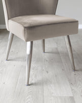 Modern dining chair with a taupe velvet upholstery and tapered metallic legs, placed on a light wooden floor.