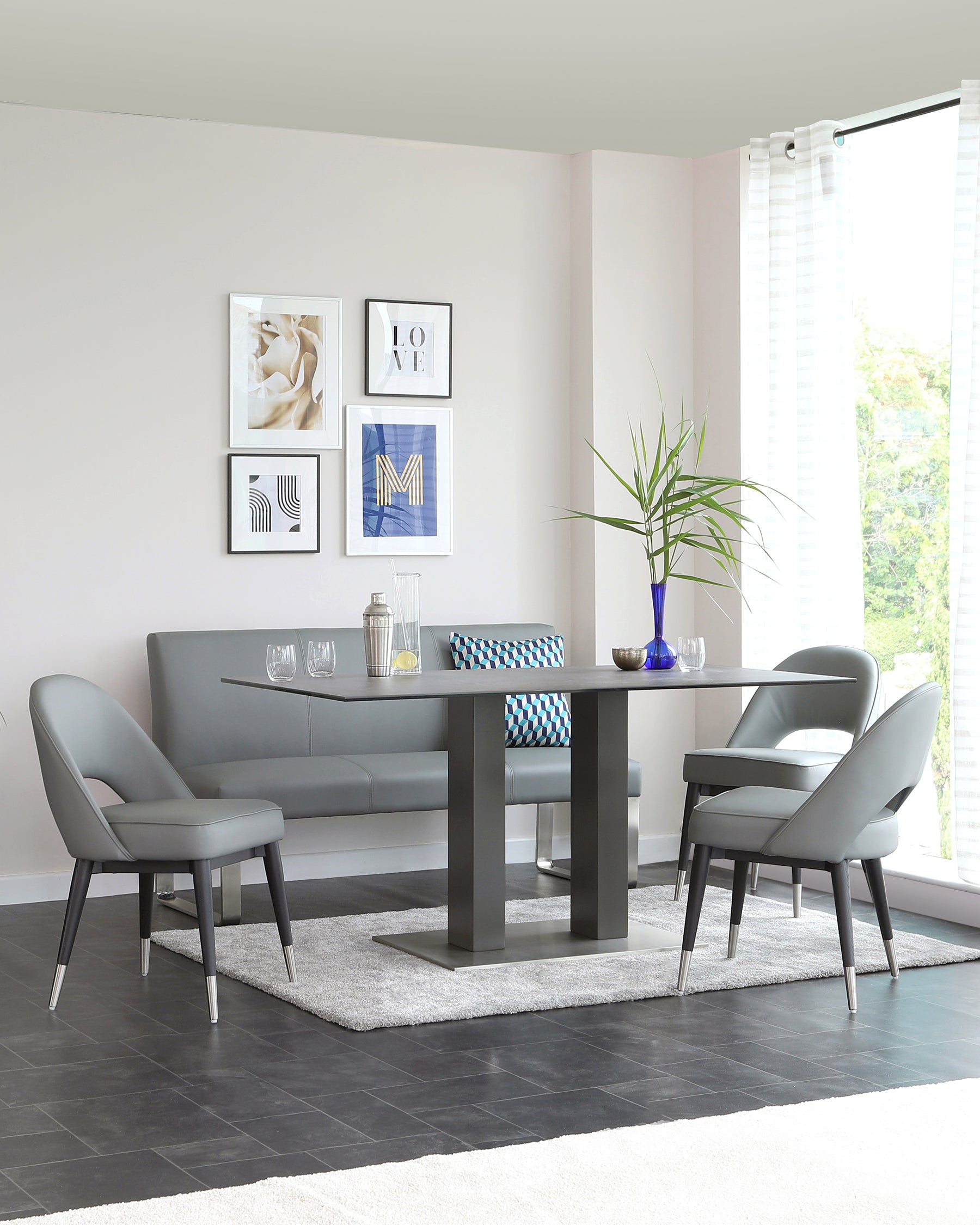 Modern dining room set including a rectangular table with a sleek dark grey surface and sturdy black square legs. Accompanied by four elegant grey upholstered chairs with slanted metal legs, and one matching dining bench with a comfortable backrest, positioned on a plush grey area rug.